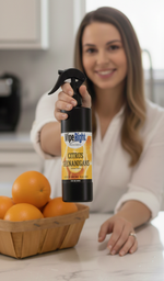 Woman holding a bottle of Wipe Right Citrus Cleaner on a kitchen counter with oranges.