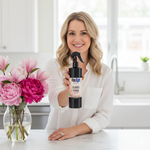 Woman holding a bottle of 'Flower Power' cleaner next to a vase of pink flowers in a kitchen.